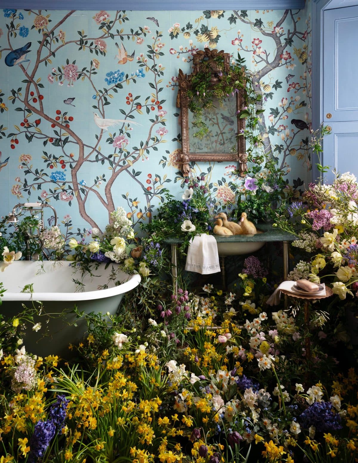 A room hung with hand-painted wallpaper and filled with spring flowers around a roll-top bath, an LVF installation.