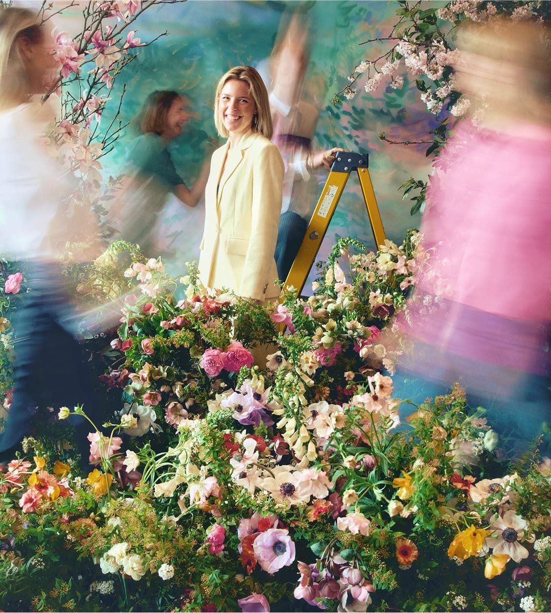 The LVF team in the studio, blurred in motion around a floral installation while one team member stands still at the centre.